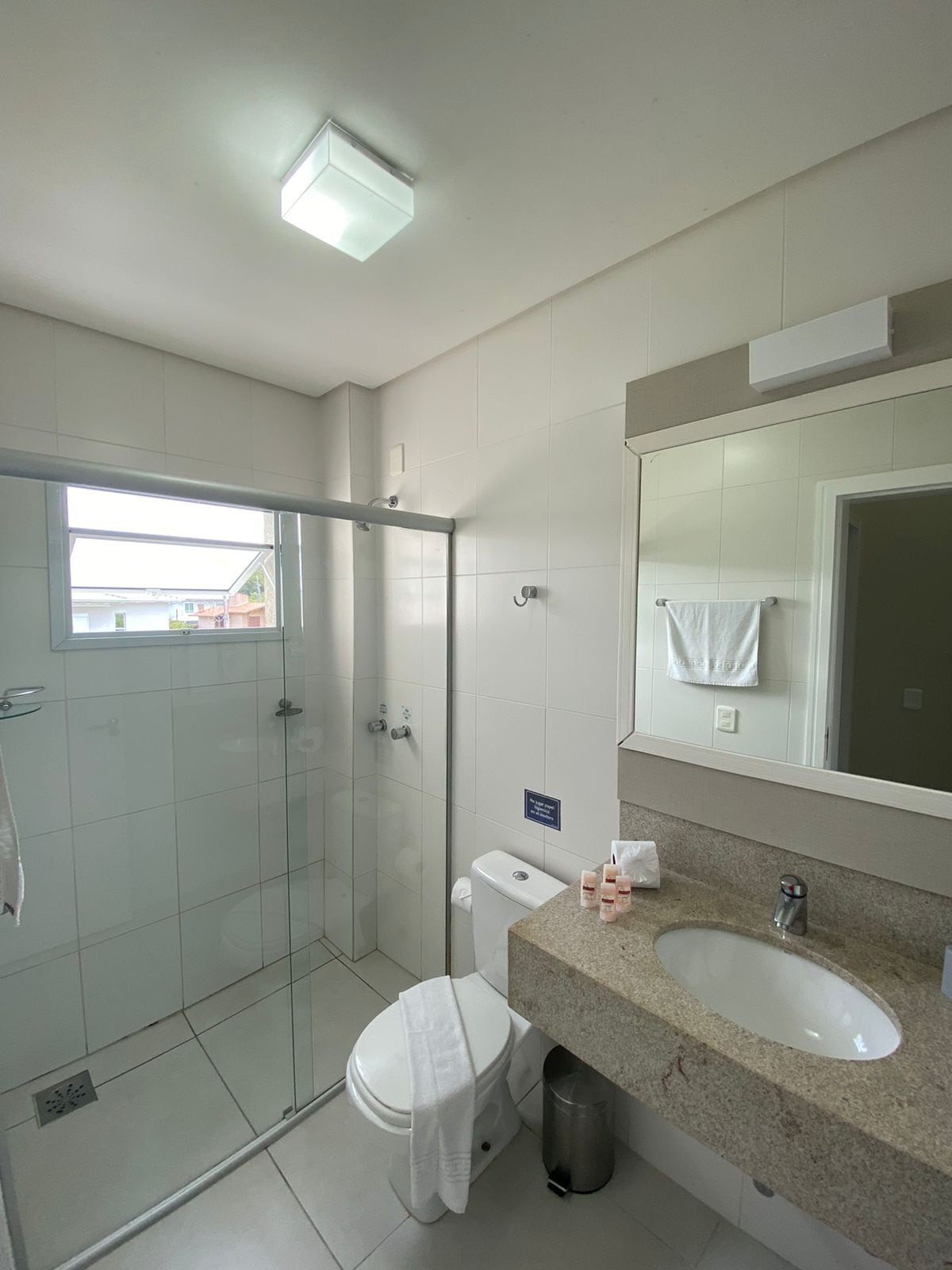 A modern bathroom with a glass-enclosed shower, a toilet, a sink with a mirror, and a towel hanging on the wall.