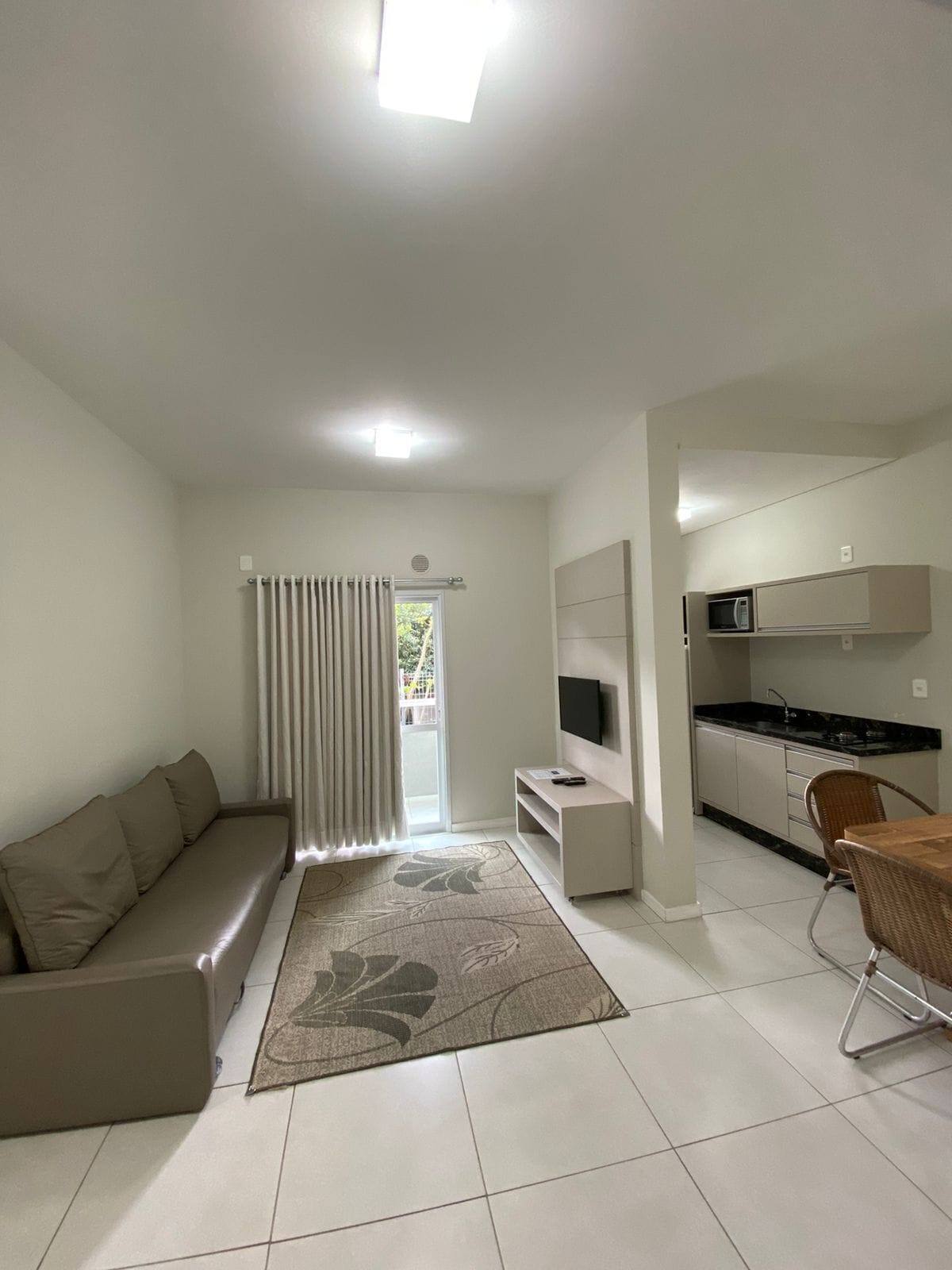 A modern living room with a sofa, a TV, a kitchen area with a microwave, and a dining table with chairs.