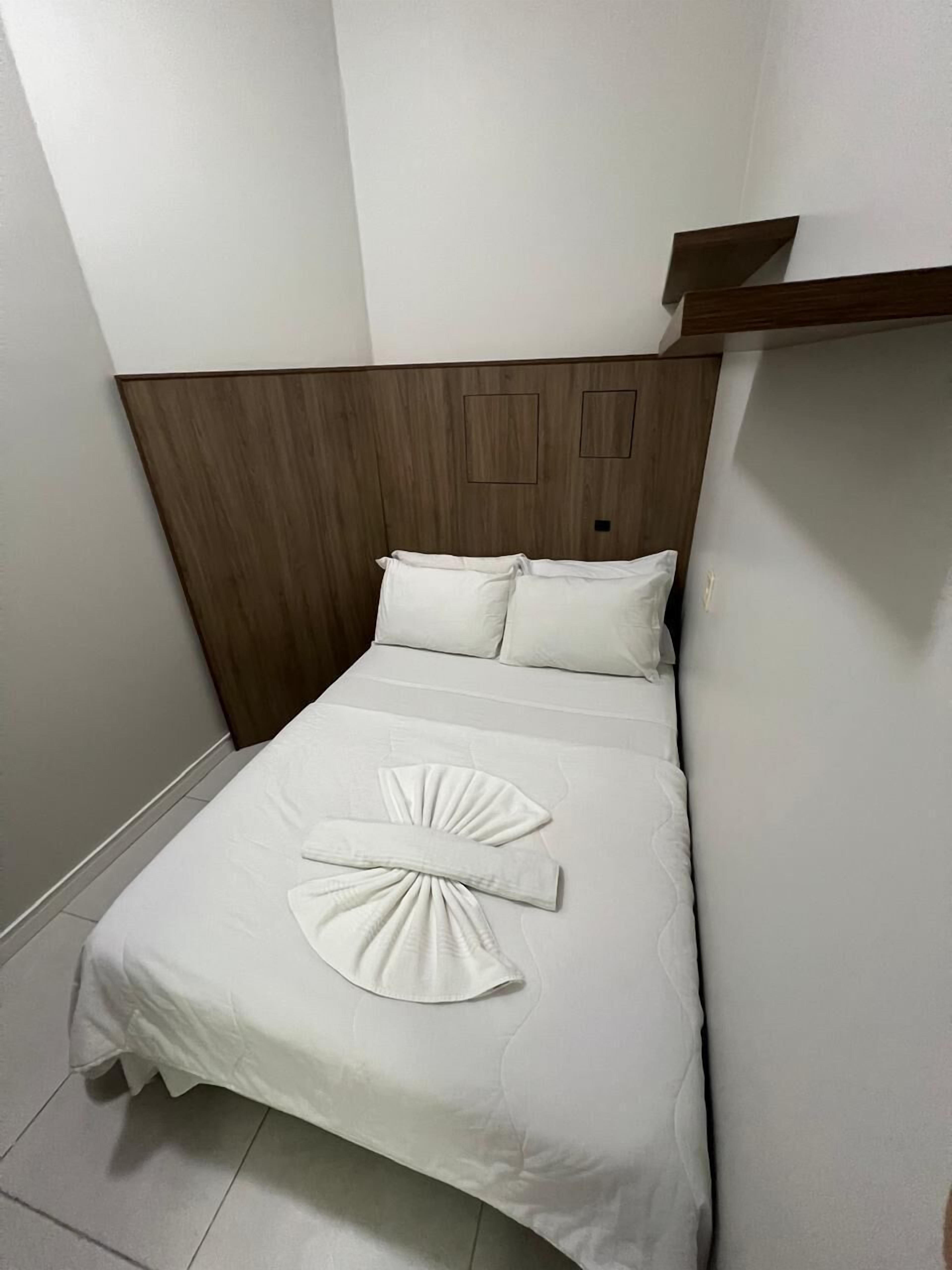 A neatly made bed with white linens and a towel arranged in a fan shape.
