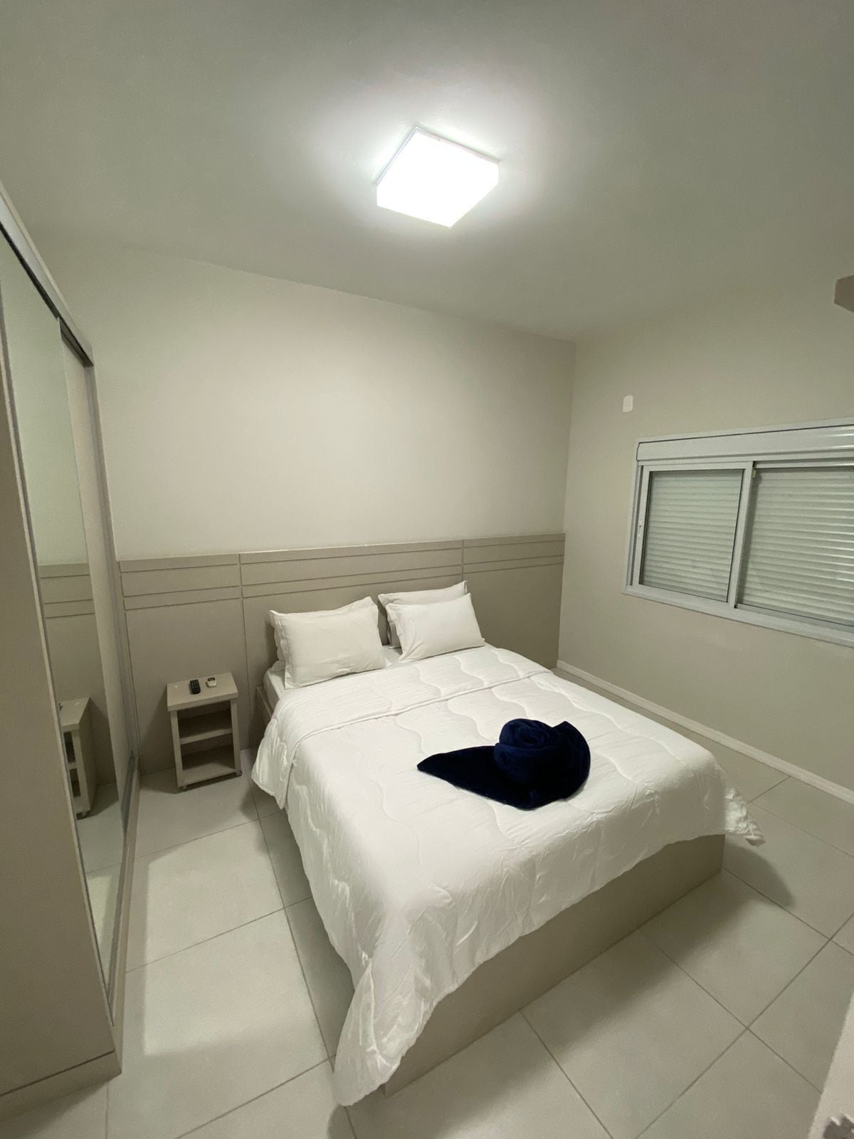 Une chambre à coucher avec un lit, une table de chevet, un miroir et une fenêtre avec des stores.