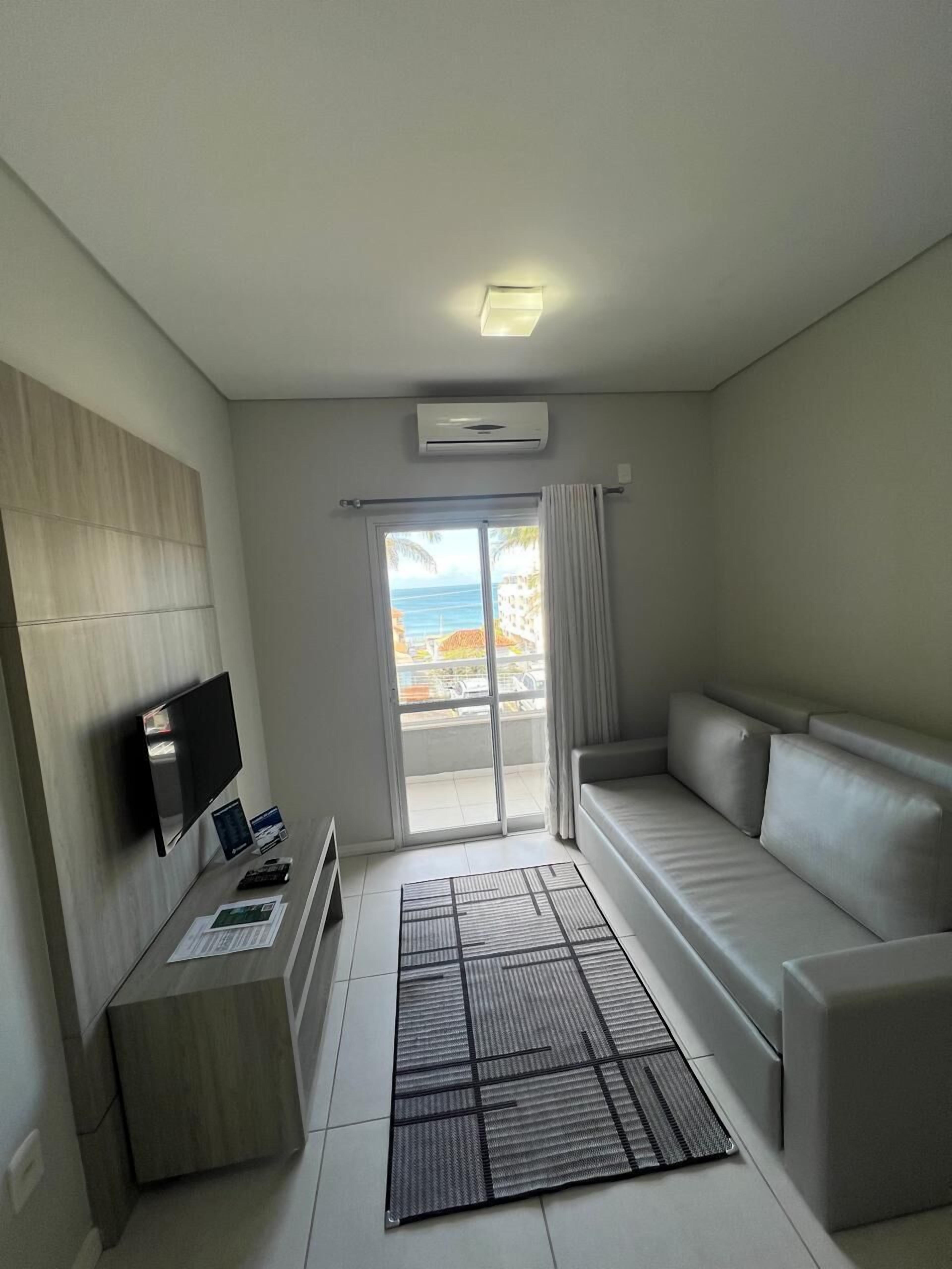Un soggiorno moderno con una televisione a schermo piatto, un divano, un tavolino e vista sull'oceano attraverso una porta-finestra in vetro.