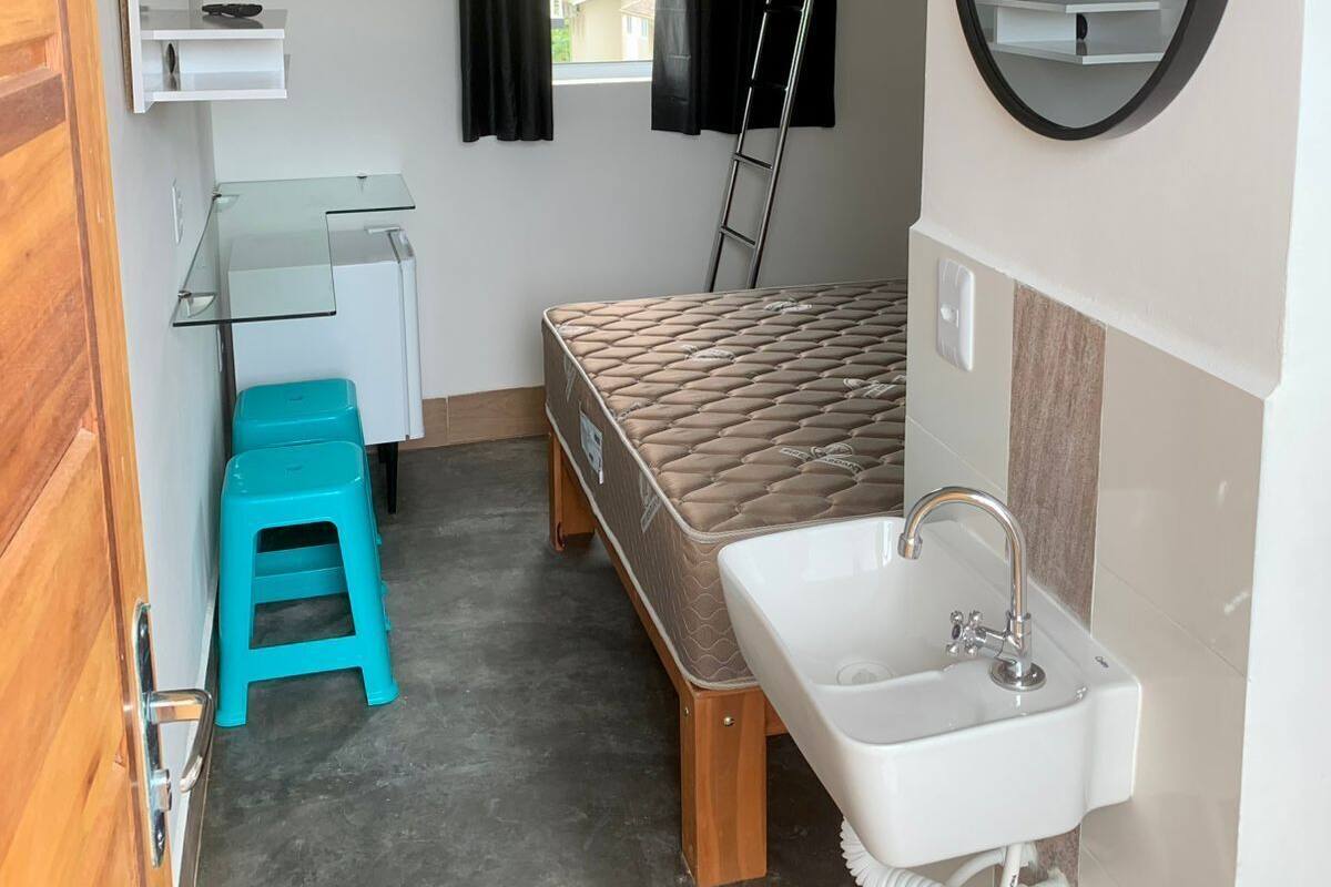 A compact room with a bed, a small desk, a sink, and a TV mounted on the wall.