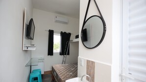 Une petite chambre comprenant un lit, un petit bureau, un miroir, un lavabo et une fenêtre avec des rideaux.