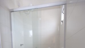 Une salle de bain avec une douche à parois de verre, des toilettes et des murs recouverts de carreaux blancs.