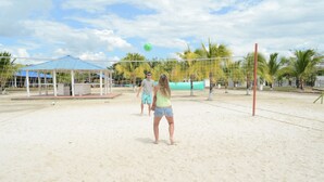 Un terrain de beach-volley avec un filet, des palmiers et une zone de sièges abritée en arrière-plan.