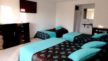 Habitación de hotel con dos camas, un aparador, un televisor y baño con espejo y lavamanos.