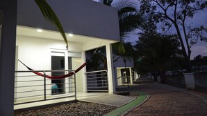 Un bâtiment moderne à l’extérieur blanc, avec un hamac rouge et un chemin pavé.