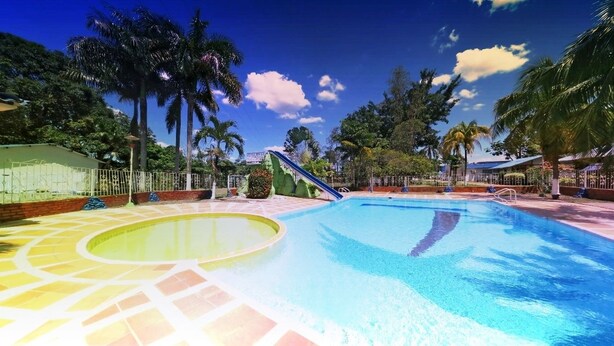 Une piscine avec une terrasse carrelée, des palmiers et un ciel bleu azur.