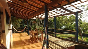Un espace extérieur abrité, doté d’une table et de chaises en bois, d’un hamac et offrant une vue sur la verdure.