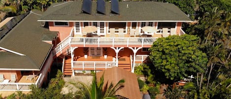 A two-story house with a balcony, solar panels on the roof, and a garden with various plants.