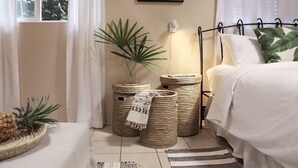 A bedroom with a bed, a bedside table with a pineapple, and three woven baskets. - Maui Garden Oasis (Lahaina)