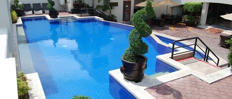 A swimming pool with tiled edges, surrounded by potted plants and outdoor seating.