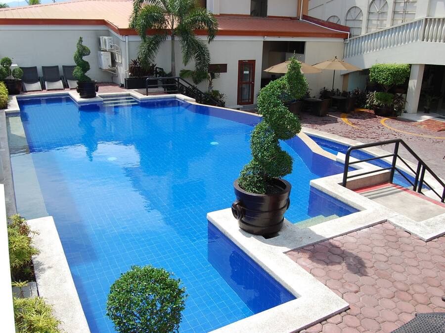 Piscina com bordas azulejadas, rodeada por plantas em vasos e mobiliário de exterior.