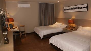 A hotel room with two single beds, a desk with a chair, a lamp, and a large window with curtains.