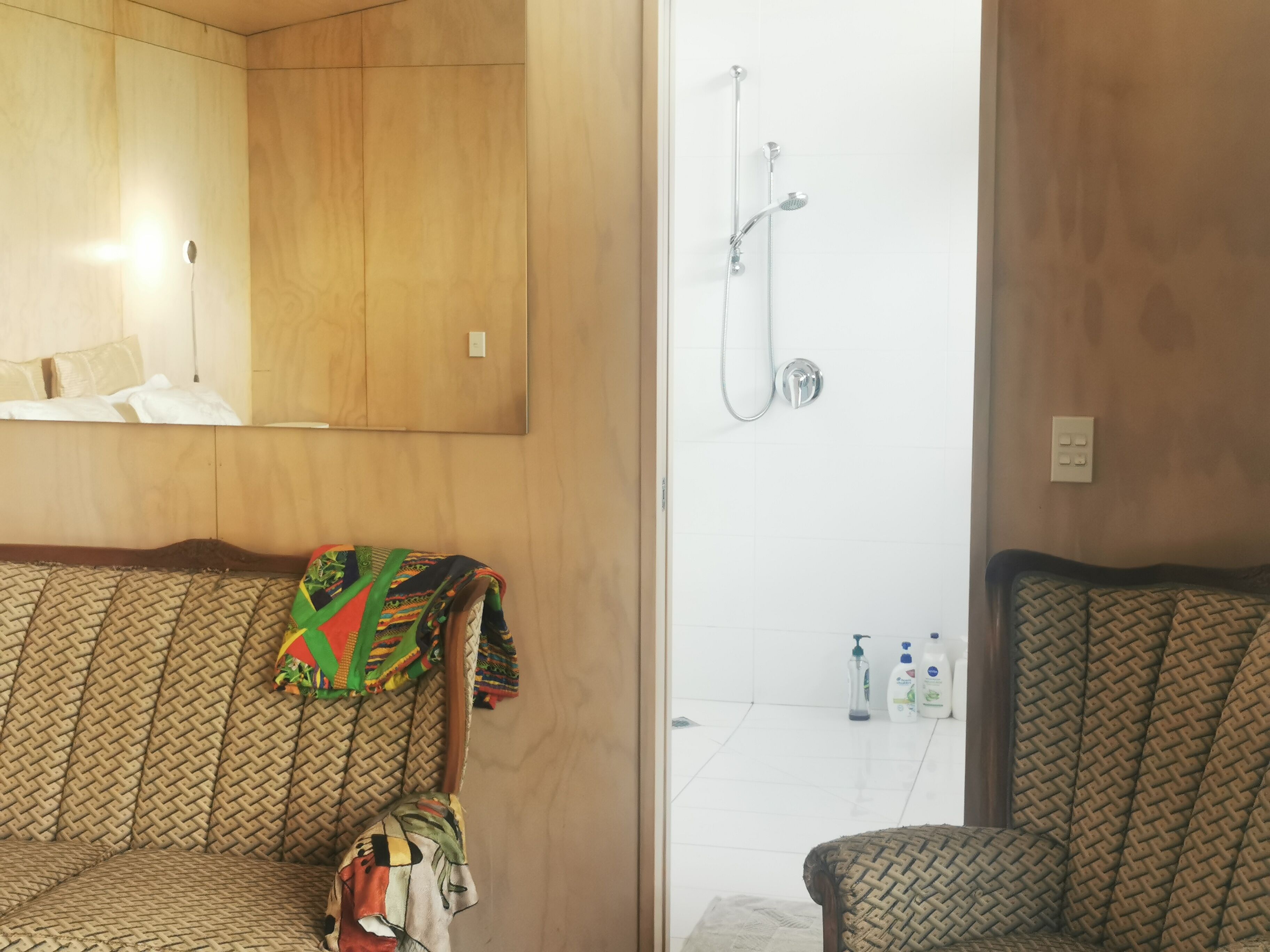 A bathroom with a wooden vanity, a shower area, and a seating area with a woven chair.