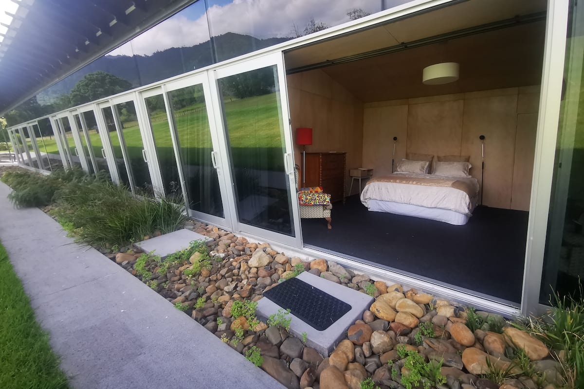 A modern hotel room with a large sliding glass door, a bed, a bedside table, and a red lamp.