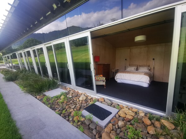 A modern hotel room with a large sliding glass door, a bed, a bedside table, and a red lamp.