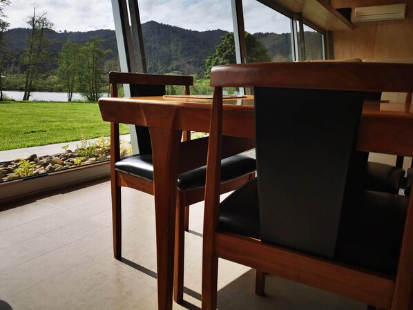 Een houten eettafel met twee stoelen, uitzicht op een meer en een bergachtig landschap door grote ramen.