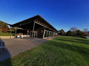 A covered outdoor dining area with tables and chairs, a grill, and a view of a lake.