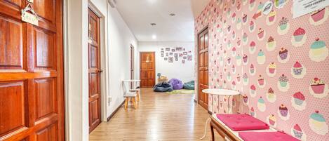 A hallway with wooden doors, a bench with pink cushions, and a wall with cupcake patterns.
