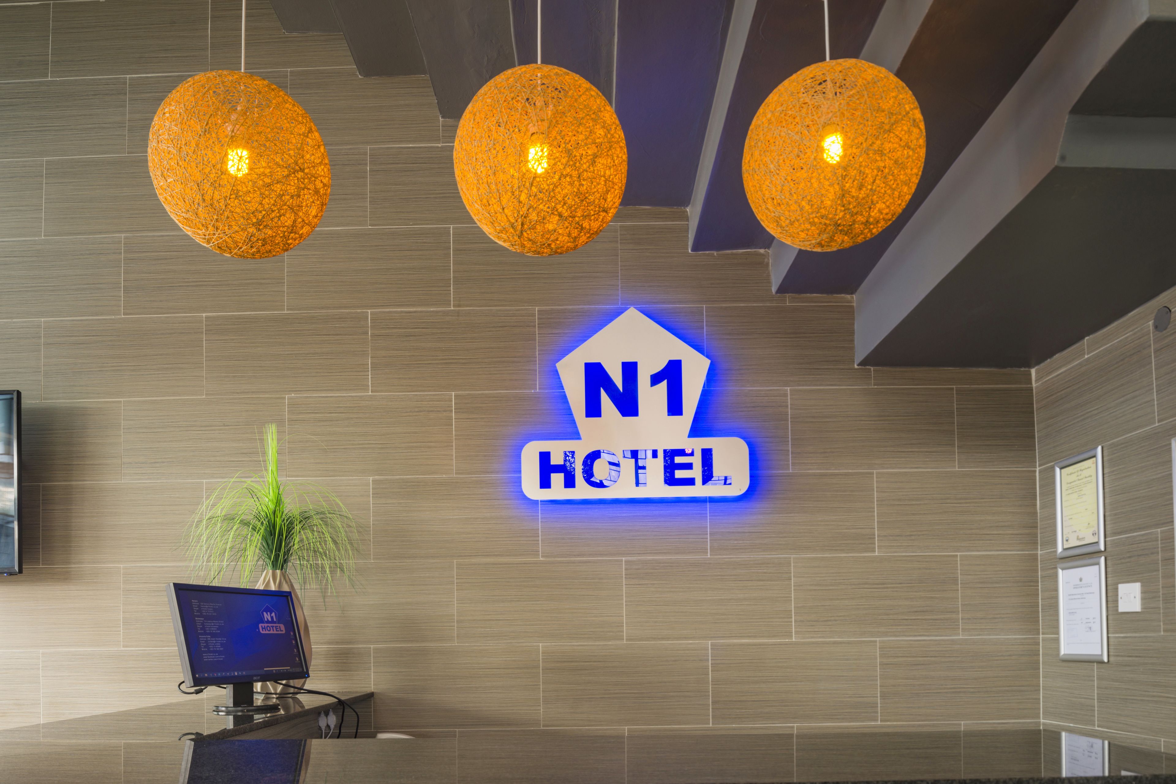 Zona de recepción con pantalla digital, cartel del Hotel N1 y tres lámparas esféricas colgantes.