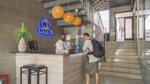 A hotel reception desk with a sign indicating it's the N1 Hotel. There are two bar stools, a potted plant, and a staircase in the background. - The N1 Hotel Bulawayo (Bulawayo)