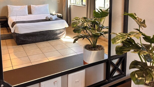 A hotel room with a bed, a cityscape painting, a ceiling fan, and a window with curtains. - The N1 Hotel Bulawayo (Bulawayo)