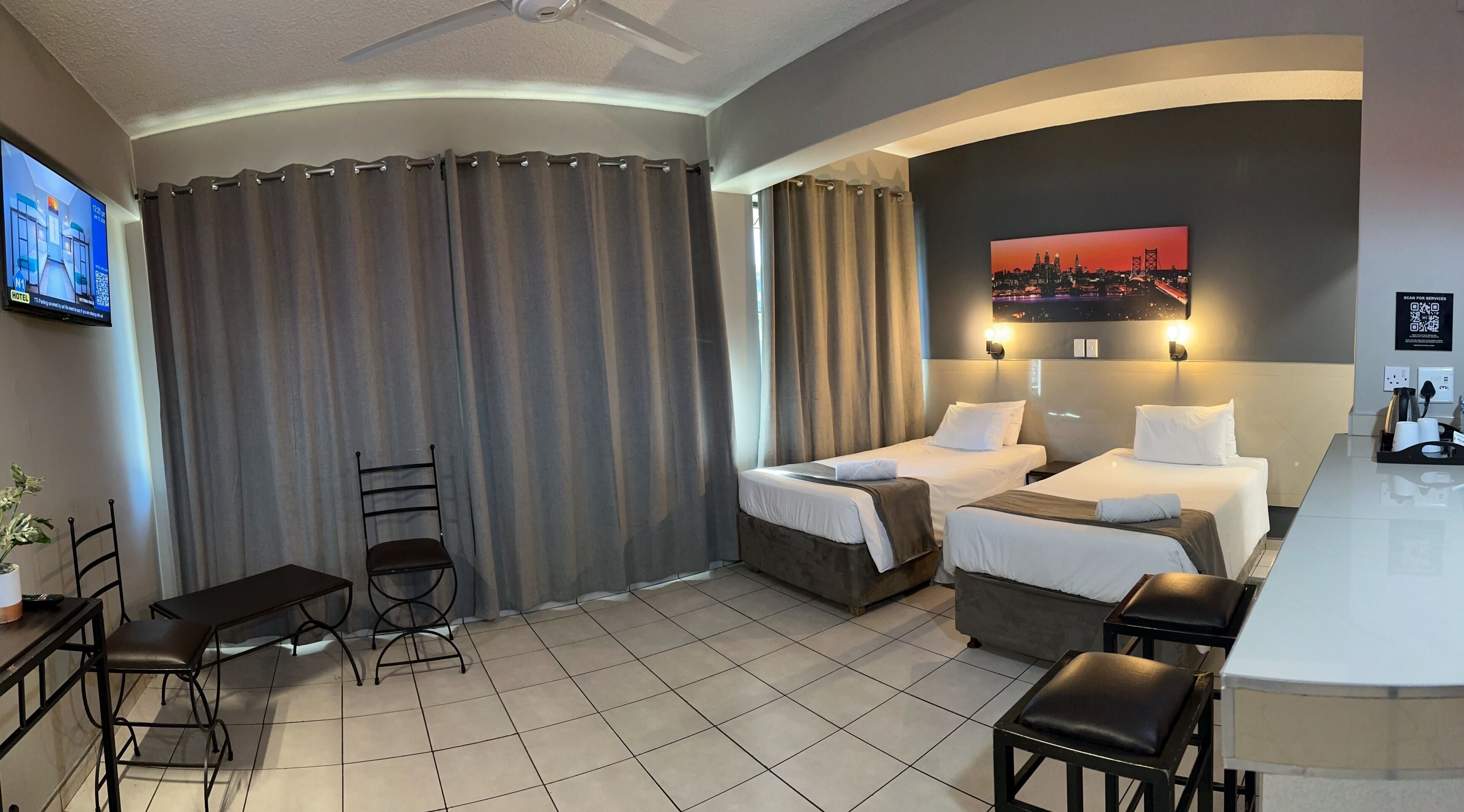 Habitación de hotel con dos camas, un escritorio, una silla, un televisor y un cuadro en la pared.