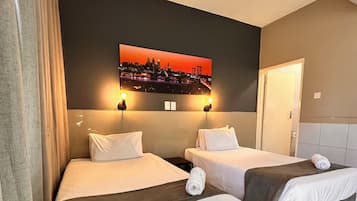 A hotel room with two beds, a cityscape painting on the wall, and a door to the right.