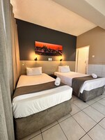 A hotel room with two beds, a cityscape painting on the wall, and a door to the right.