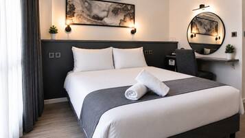 A hotel room with a bed, a bedside table, a chair, a mirror, and a wall-mounted air conditioner.