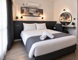 Habitación de hotel con cama, mesita de noche, silla, espejo y aire acondicionado instalado en la pared.