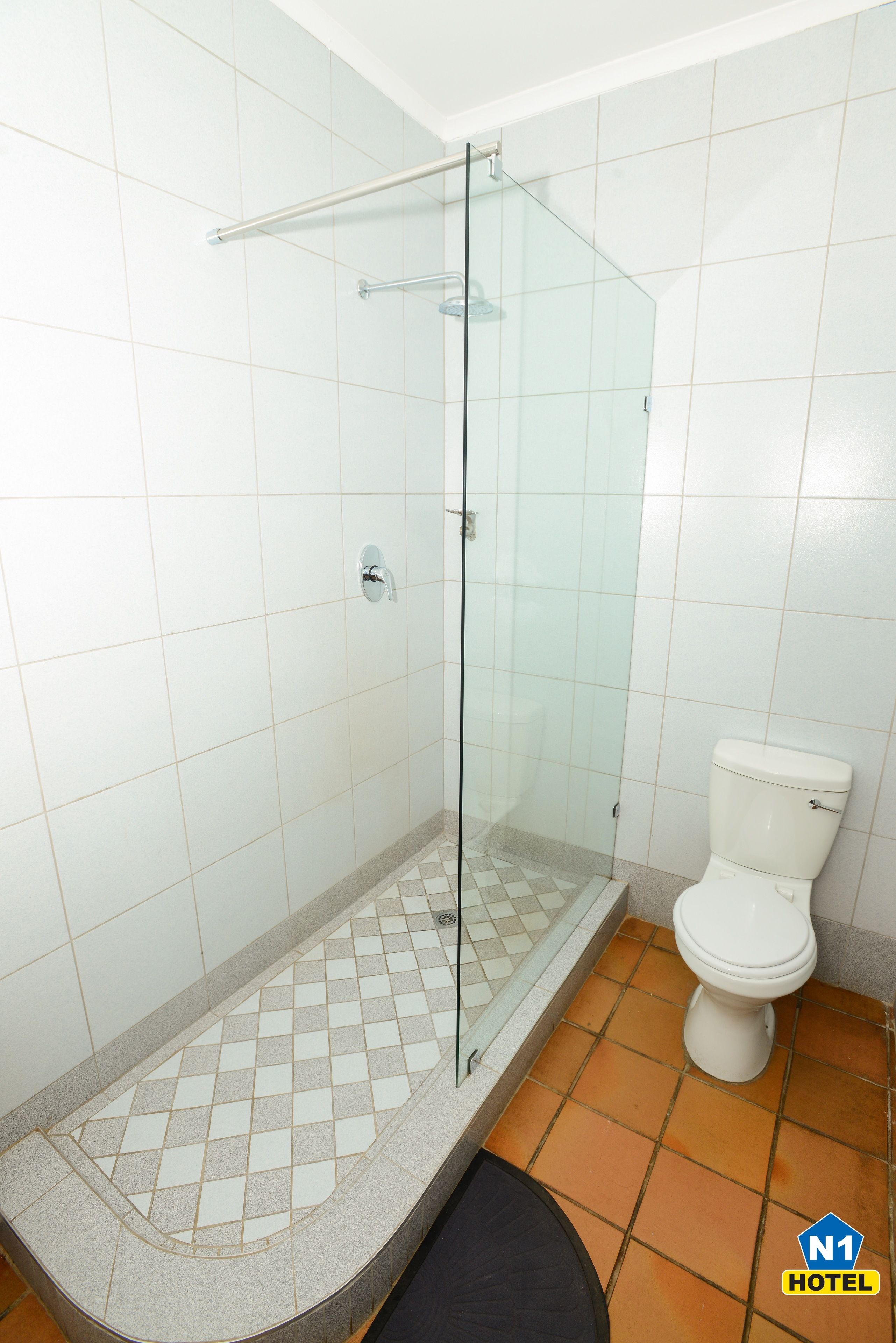 Une salle de bain avec une douche à parois de verre, des toilettes et un carrelage au sol.