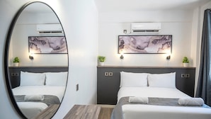 Een hotelkamer met twee bedden, een grote spiegel, wandunits voor airconditioning en twee wandlampen.