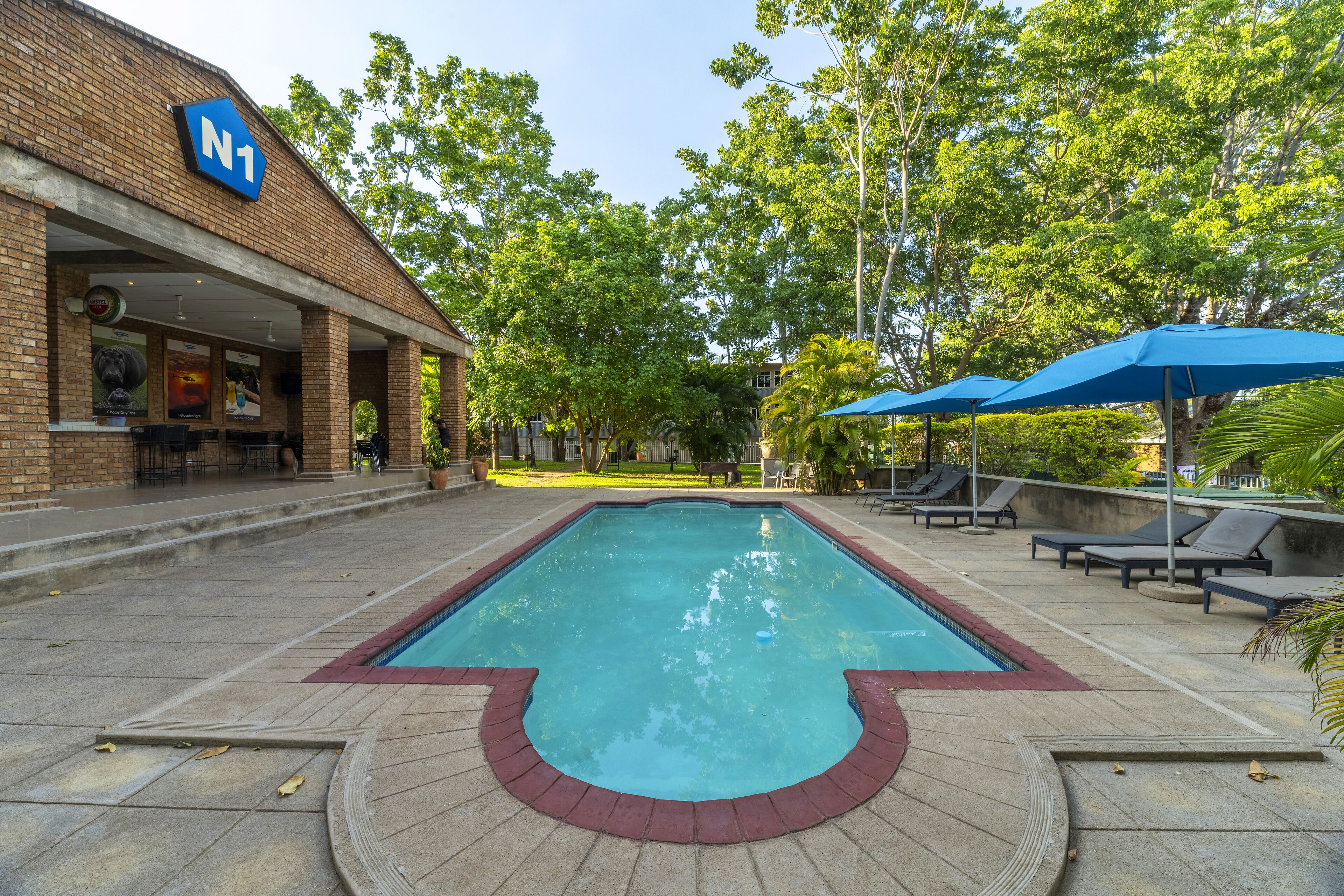 A swimming pool with a brick border, lounge chairs, and umbrellas.