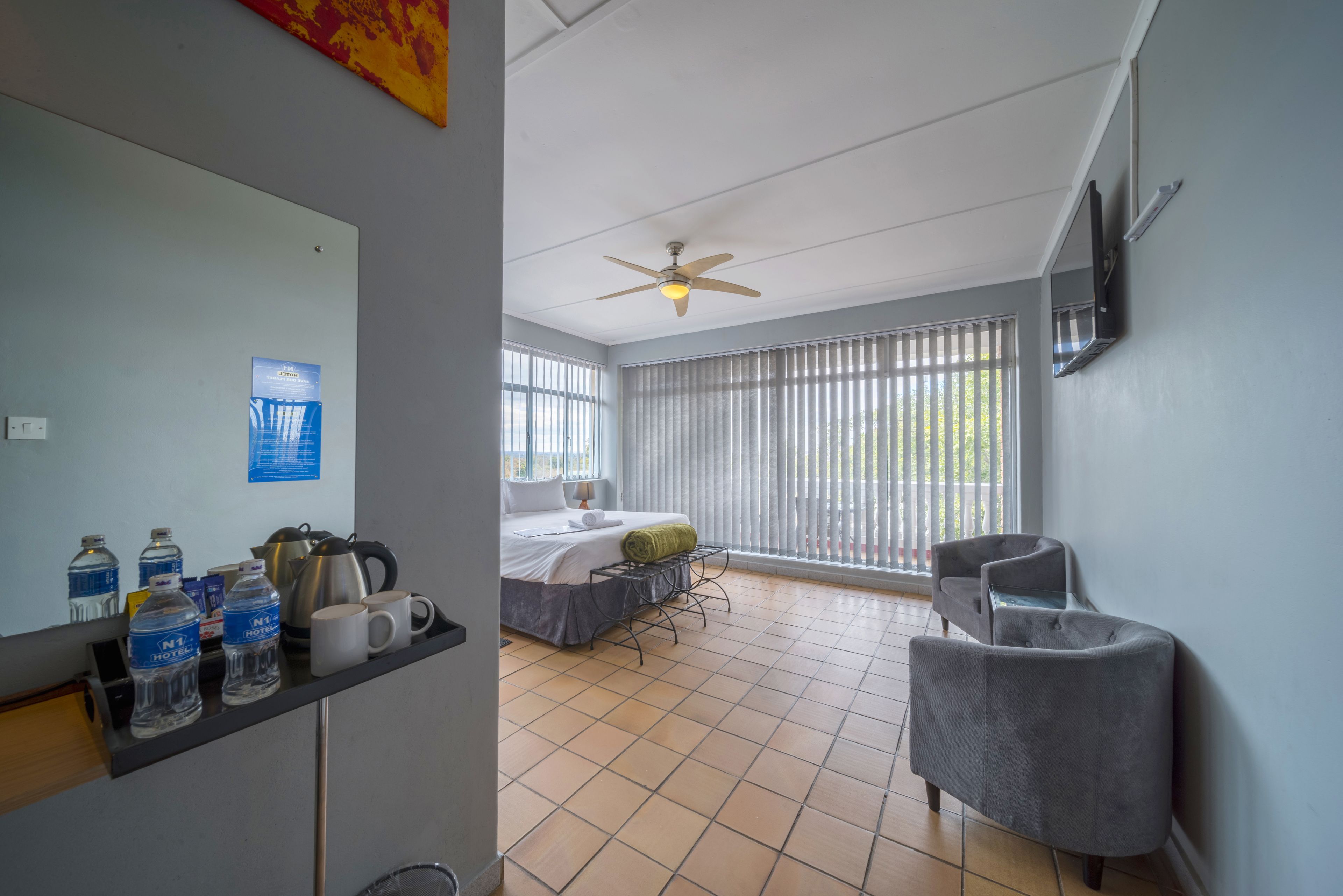 Una habitación de hotel con una cama, un escritorio con botellas de agua, una tetera y una silla.