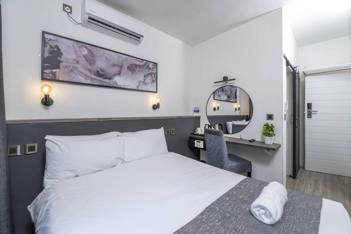 Una habitación de hotel con cama, mesita de noche, silla y un espejo grande.