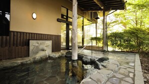 Zona de aguas termales naturales de piedra con una terraza de madera, pared de piedra y cerca de madera.