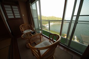 A balcony with wicker chairs and a small table, overlooking a green area with a fence.