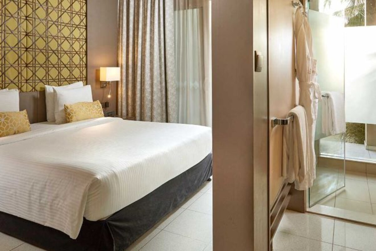 A hotel room with a bed, a bathroom with a glass shower, and a patterned wall.