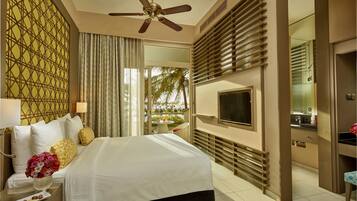 Habitación de hotel con cama, televisión, ventilador de techo, ventana con cortinas y vista a palmeras.