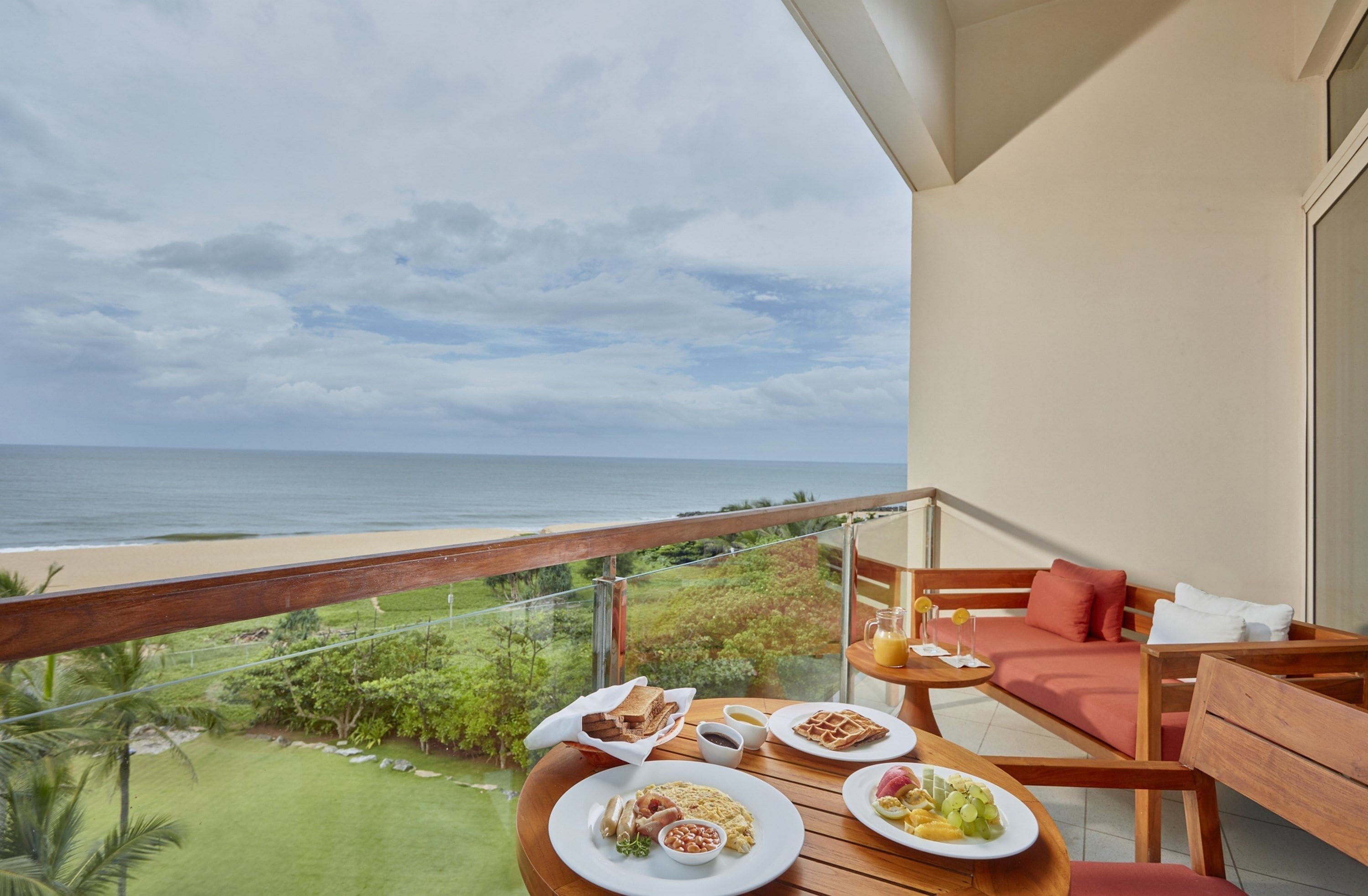 A balcony with a table set for breakfast, overlooking a beach and ocean.