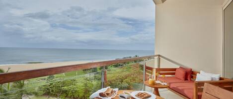 A balcony with a table set for breakfast, overlooking a beach and ocean.