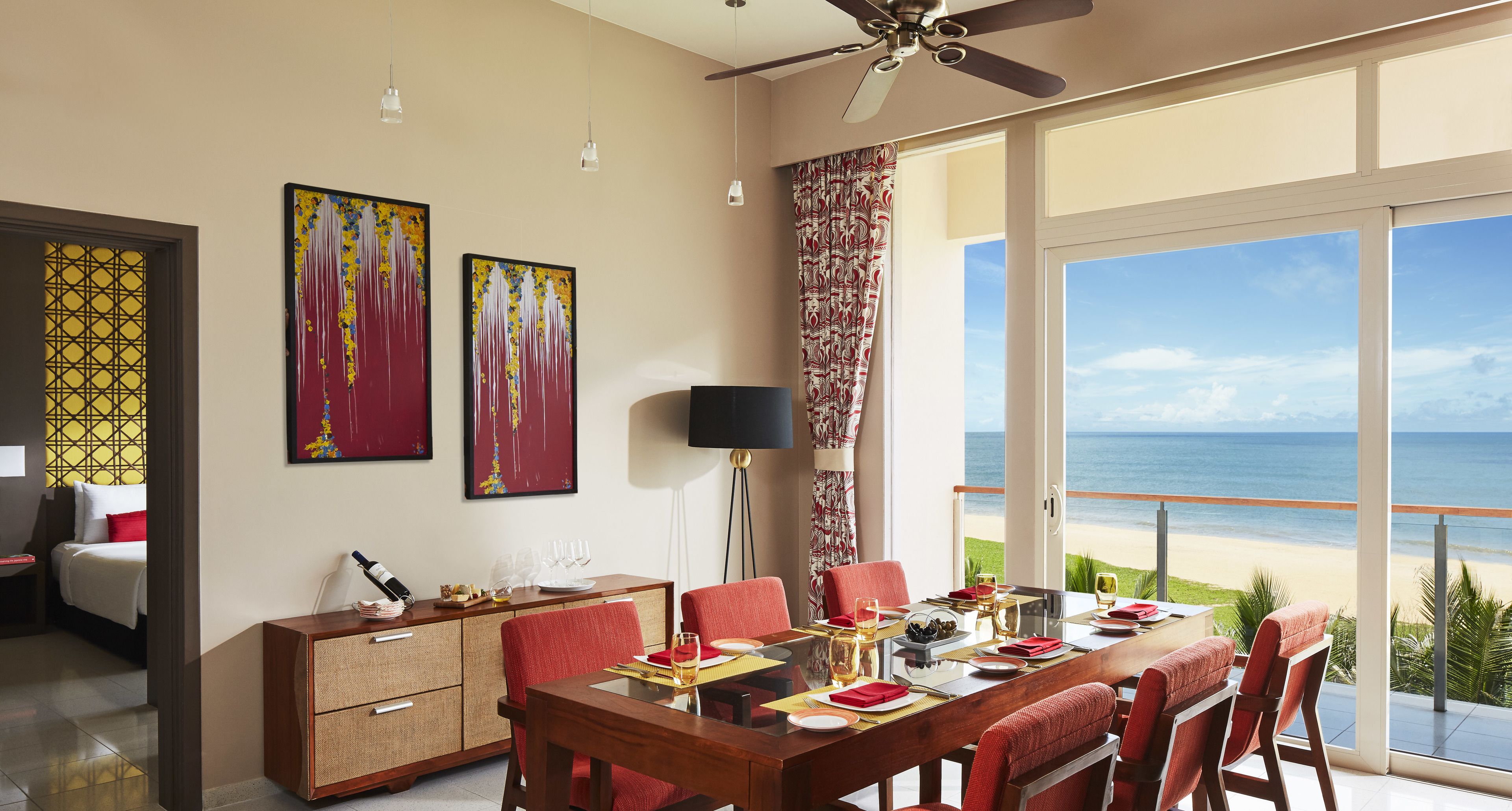 A dining area with a table set for four, a ceiling fan, and a view of the beach.
