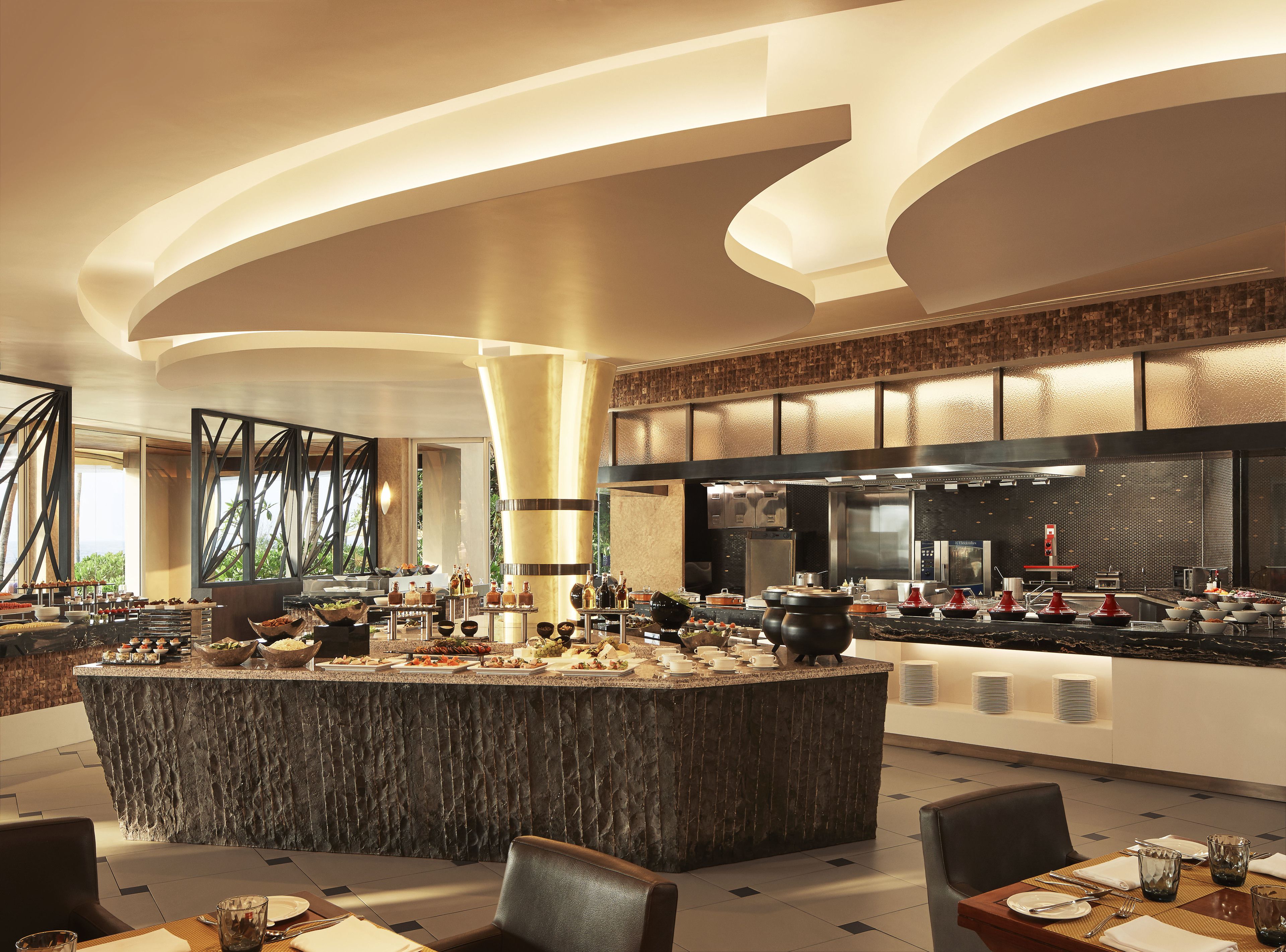 A modern restaurant with a central island bar, a kitchen area, and seating arrangements.