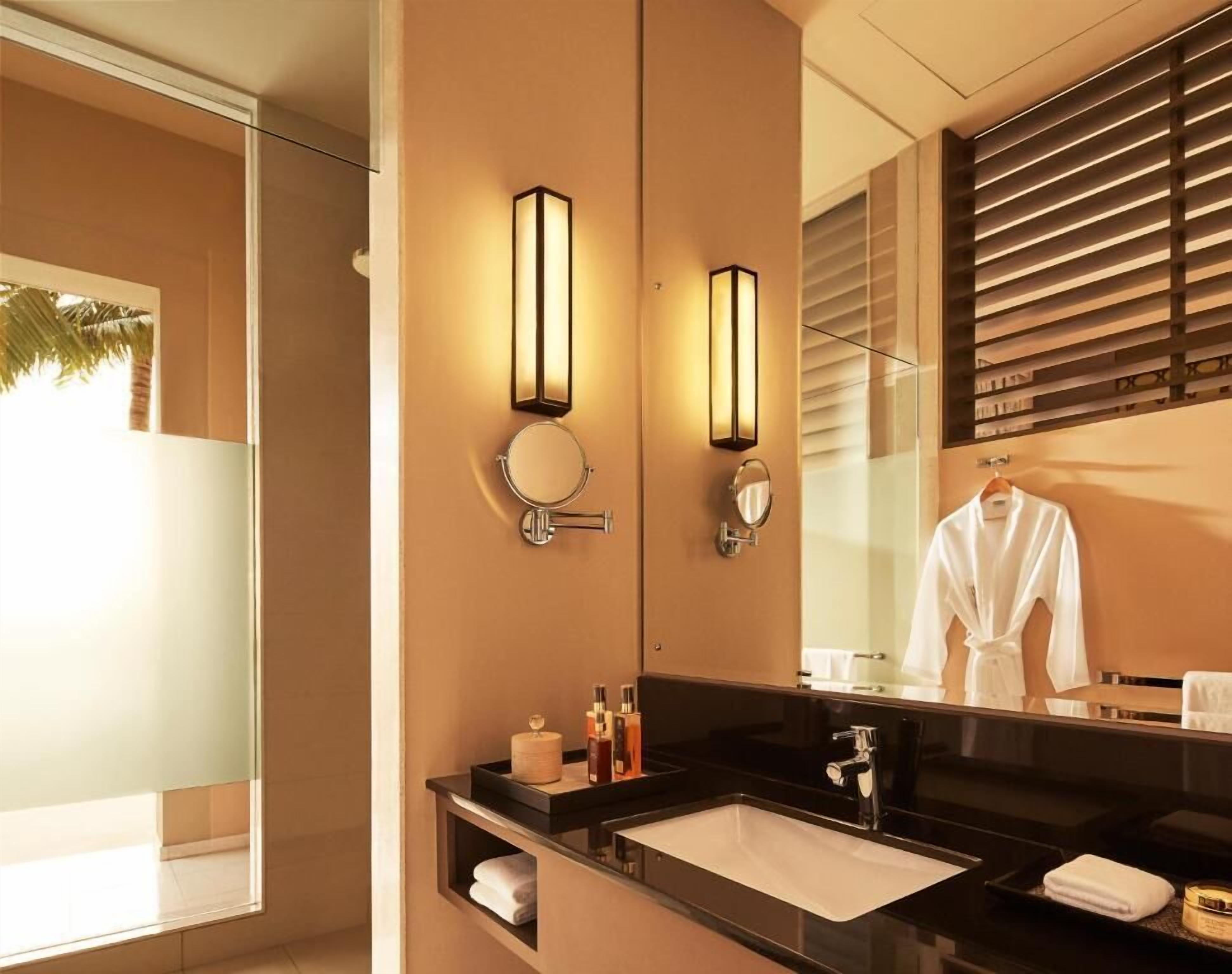 A modern bathroom with a large mirror, two wall-mounted lights, a sink, and a towel rack.
