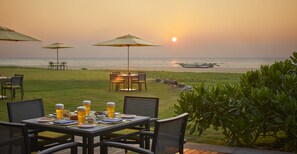 An outdoor dining area with tables and chairs, overlooking the ocean at sunset.
