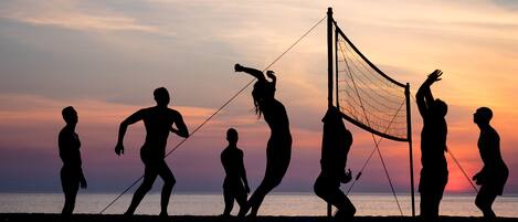 Silhouettes of people playing volleyball at sunset.