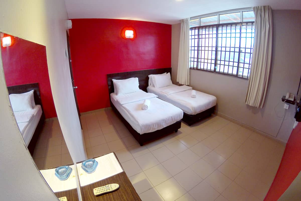 Habitación de hotel con dos camas individuales, una mesita con un control remoto y una ventana con barrotes.