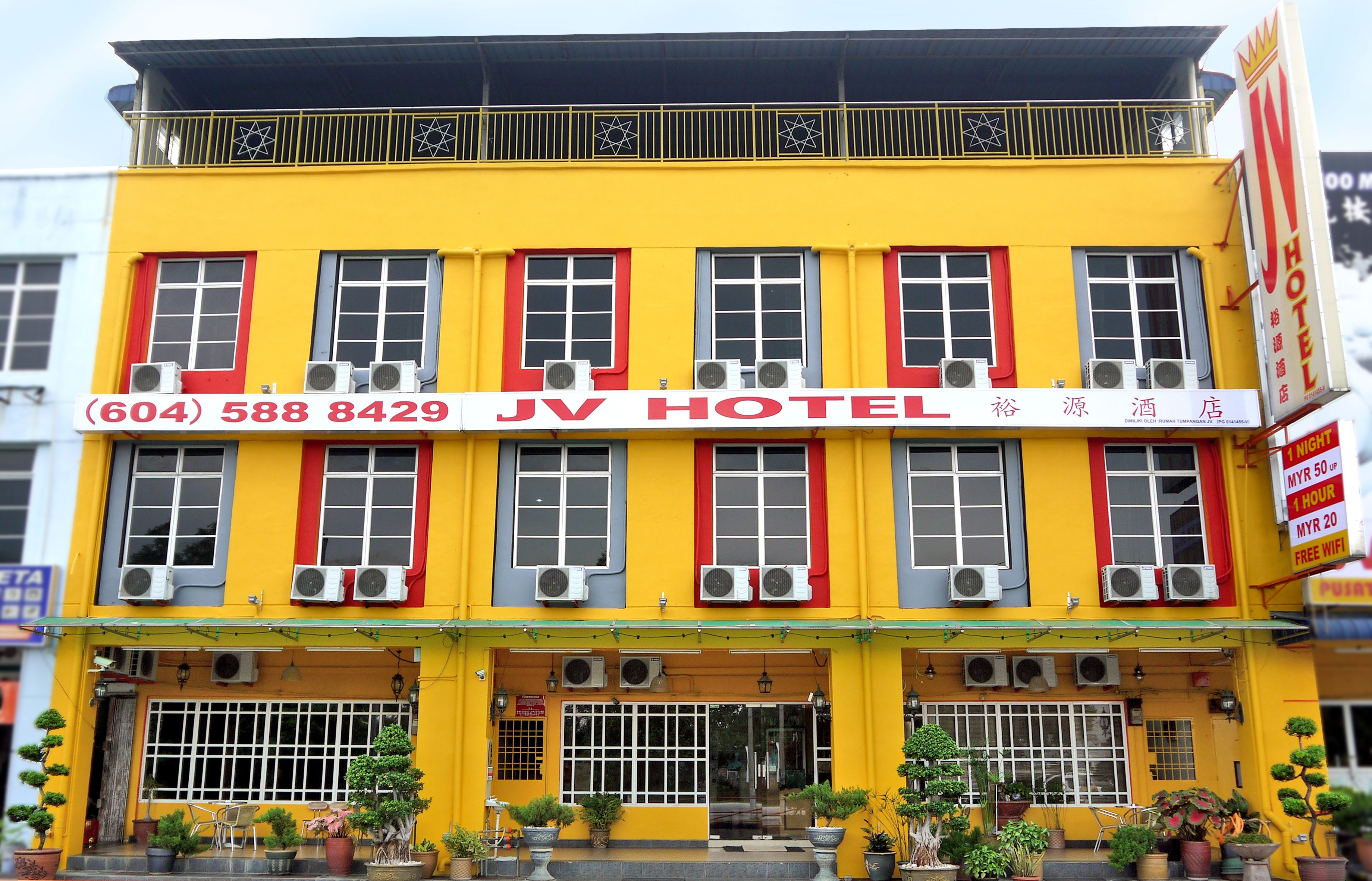 Un hotel con fachada amarilla, marcos de ventanas rojos y varias unidades de aire acondicionado.
